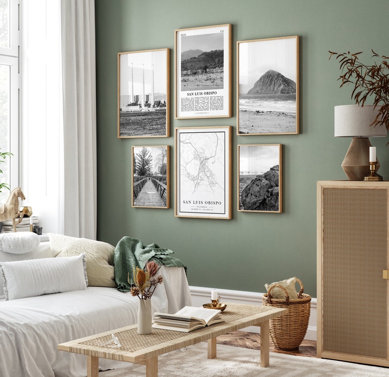 May include: A living room with a white couch and a wooden coffee table. The wall is painted a light green color and has six black and white framed photographs of San Luis Obispo, California. The photographs include a beach scene, a map of the city, and a view of the city from the ocean.