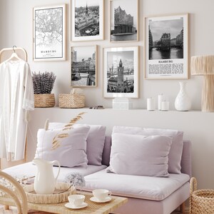 May include: A living room with a light purple sofa, a coffee table, and a wall with black and white framed prints of Hamburg, Germany. The prints include a map, a cityscape, and a building.
