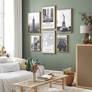 May include: A set of six framed black and white prints depicting New York City landmarks. The images show the Empire State Building, Times Square, the Statue of Liberty, Brooklyn Bridge, a map, and Central Park. The frames are a light wood colour.