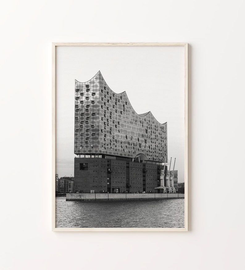 May include: A black and white photograph of a modern building with a unique, angular design. The building is situated on a waterfront with cranes in the background.