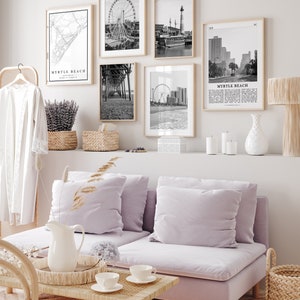 May include: A living room with a light purple sofa, a coffee table, and a white vase with a floral design. There are five black and white framed photos on the wall above a shelf with candles and a white vase. The photos depict various scenes from Myrtle Beach, South Carolina, including a Ferris wheel, a pier, a lighthouse, and a street scene.