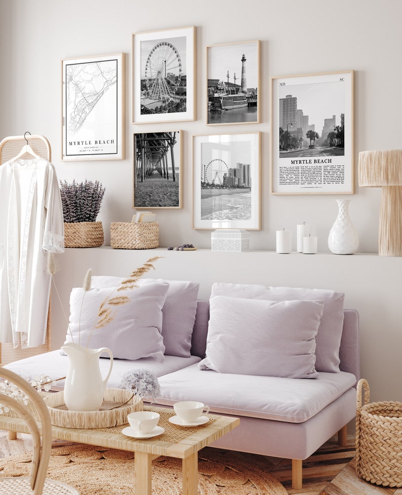 May include: A living room with a light purple sofa, a coffee table, and a white vase with a floral design. There are five black and white framed photos on the wall above a shelf with candles and a white vase. The photos depict various scenes from Myrtle Beach, South Carolina, including a Ferris wheel, a pier, a lighthouse, and a street scene.