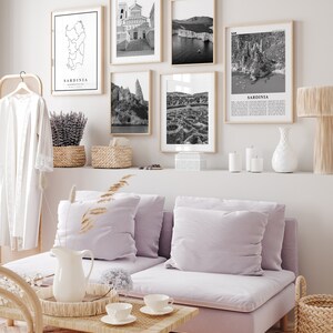 May include: A living room interior with a light purple sofa, a coffee table, and a wall gallery of black and white photos of Sardinia, Italy. The photos include a map of Sardinia, a church, a rocky coastline, and a view of the island's interior.
