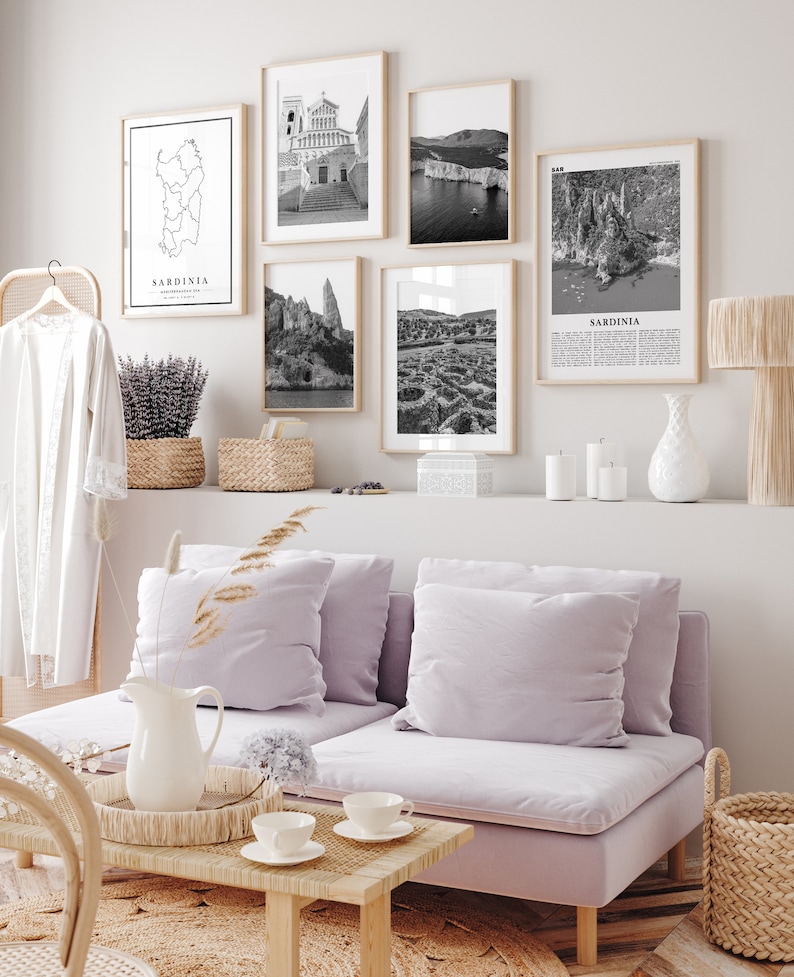 May include: A living room interior with a light purple sofa, a coffee table, and a wall gallery of black and white photos of Sardinia, Italy. The photos include a map of Sardinia, a church, a rocky coastline, and a view of the island's interior.