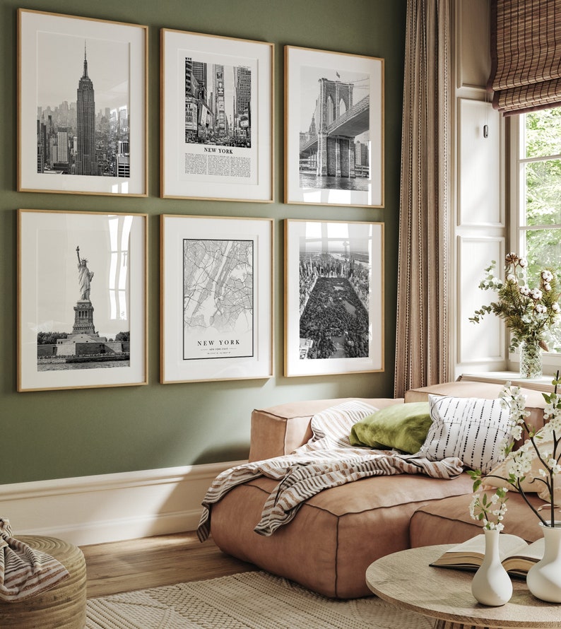 May include: Six framed monochrome prints of New York City landmarks displayed on a green wall. The prints show the Empire State Building, Times Square, the Brooklyn Bridge, the Statue of Liberty, a city map, and Central Park. The frames are gold-coloured.