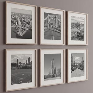 Puede incluir: Seis fotografías enmarcadas en blanco y negro de paisajes urbanos y arquitectura. Las imágenes incluyen vistas aéreas de ciudades, puentes y edificios. Los marcos son de madera clara con paspartús blancos.