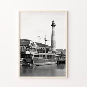 May include: Black and white photograph of a lighthouse and a boat docked at a waterfront restaurant called "Margaritaville".