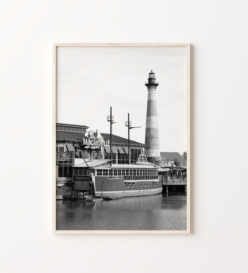 May include: Black and white photograph of a lighthouse and a boat docked at a waterfront restaurant called "Margaritaville".
