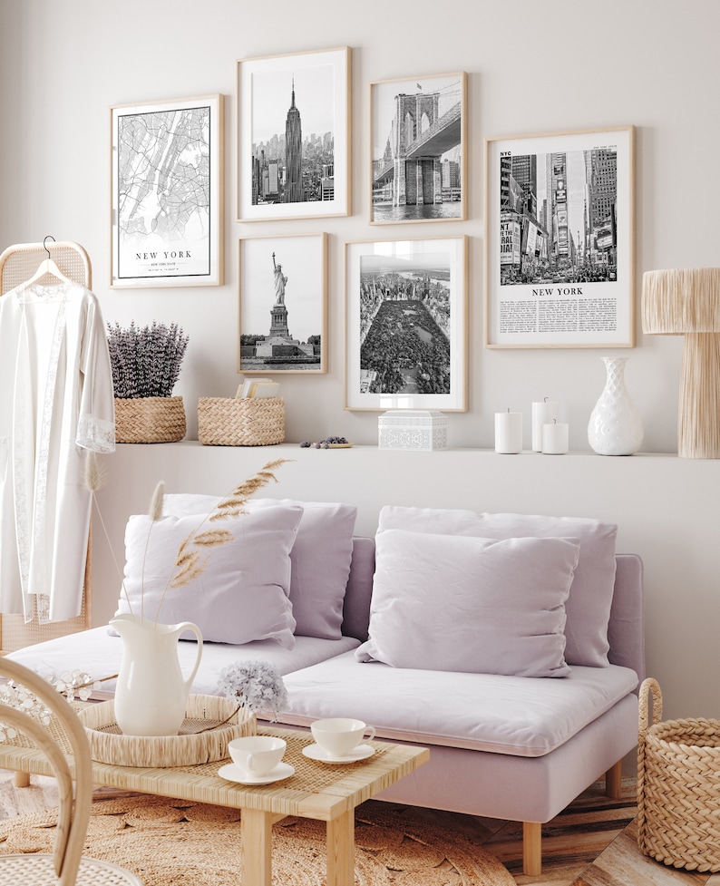 May include: A living room with framed black and white prints of New York City landmarks, such as the Empire State Building and Brooklyn Bridge. The room includes a lilac sofa, a wooden coffee table, and various decorative elements.