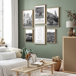 May include: A set of six black and white framed prints featuring images of Sardinia, Italy. The prints include a map of Sardinia, a church, a cliffside, and a view of the coastline. The prints are arranged in a grid pattern on a green wall.