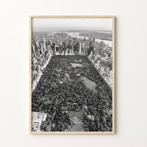 May include: Monochrome aerial photograph of Central Park in New York City, framed in light wood. The image shows the park's trees, lakes, and pathways, contrasting with the surrounding skyscrapers. The photograph captures the urban landscape.