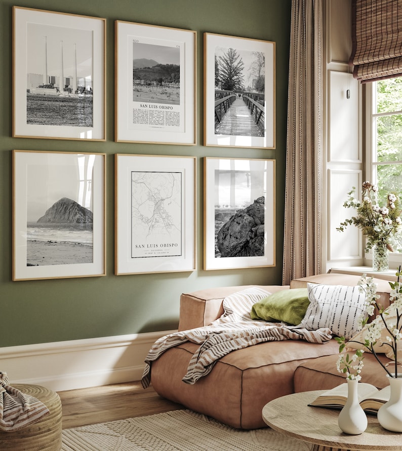 May include: A living room with a green wall and a light brown leather couch. There are six black and white framed photos on the wall, including a map of San Luis Obispo, California. The couch has a green throw pillow and a striped throw blanket.
