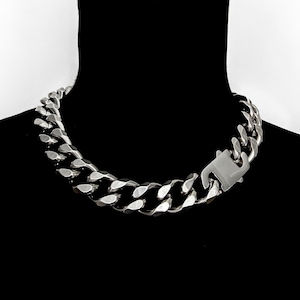Puede incluir: Un collar de cadena de eslabones gruesos en tono plateado pulido con grandes eslabones metálicos entrelazados. El collar se asegura con un prominente mecanismo de cierre mecánico de forma rectangular integrado en el diseño.