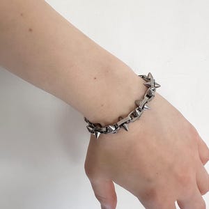 May include: A silver chain bracelet with pointed spikes. The bracelet is made of metal and has a punk rock aesthetic.