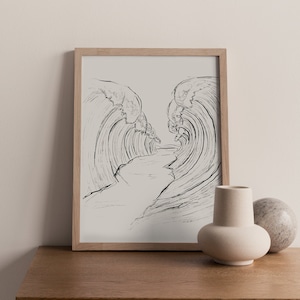 Könnte beinhalten: Ein gerahmtes Schwarzweiß-Strichzeichnung von Wellen, die aufeinanderprallen und in der Mitte einen Weg bilden. Der Rahmen ist aus hellem Holz und die Zeichnung ist auf weißem Hintergrund. Die Zeichnung befindet sich auf einem Holztisch mit einer kleinen weißen Vase und einer Steinkugel.