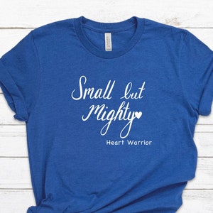 May include: A royal blue t-shirt with the text "Small but Mighty" in white with a small heart symbol. The text "Heart Warrior" is also in white below the main text.