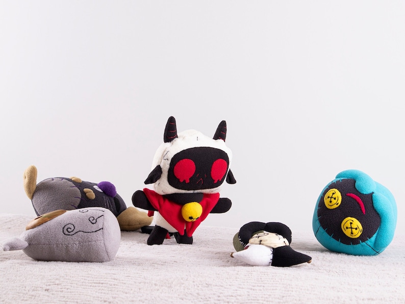 May include: Five plush toys, including a black and white character with red eyes and a red cape, a gray and white character with a swirl design, a black and gray character with a purple detail, a black and blue character with yellow buttons, and a white and black character with a black and white design.