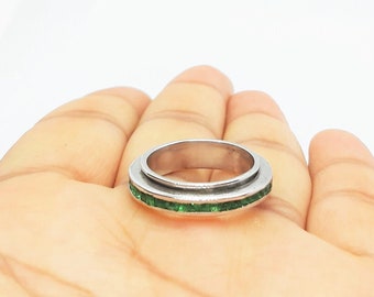 May include: A silver ring with a band of green gemstones.