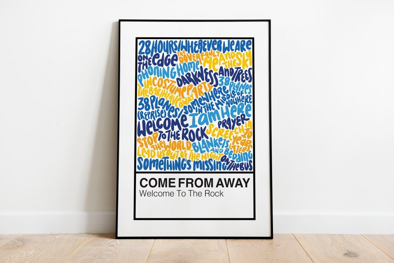 May include: A white poster with a black frame featuring a blue and yellow word cloud with the text "Come From Away" and "Welcome To The Rock".