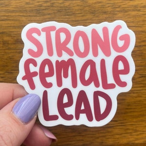 May include: A white sticker with the text "STRONG female LEAD" in pink and red lettering.