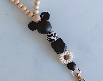May include: A wooden beaded lanyard with a Mickey Mouse charm and a daisy charm. The lanyard has the word "Mommy" spelled out in pink and gold beads.