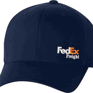 May include: A navy blue baseball cap with the FedEx Freight logo embroidered on the front in white and orange.