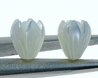 May include: Two white, carved flower-shaped beads. The beads are made of mother of pearl and have a delicate, intricate design.