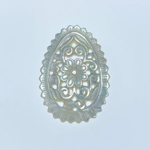 May include: A white oval-shaped mother of pearl pendant with a delicate floral design carved into it.