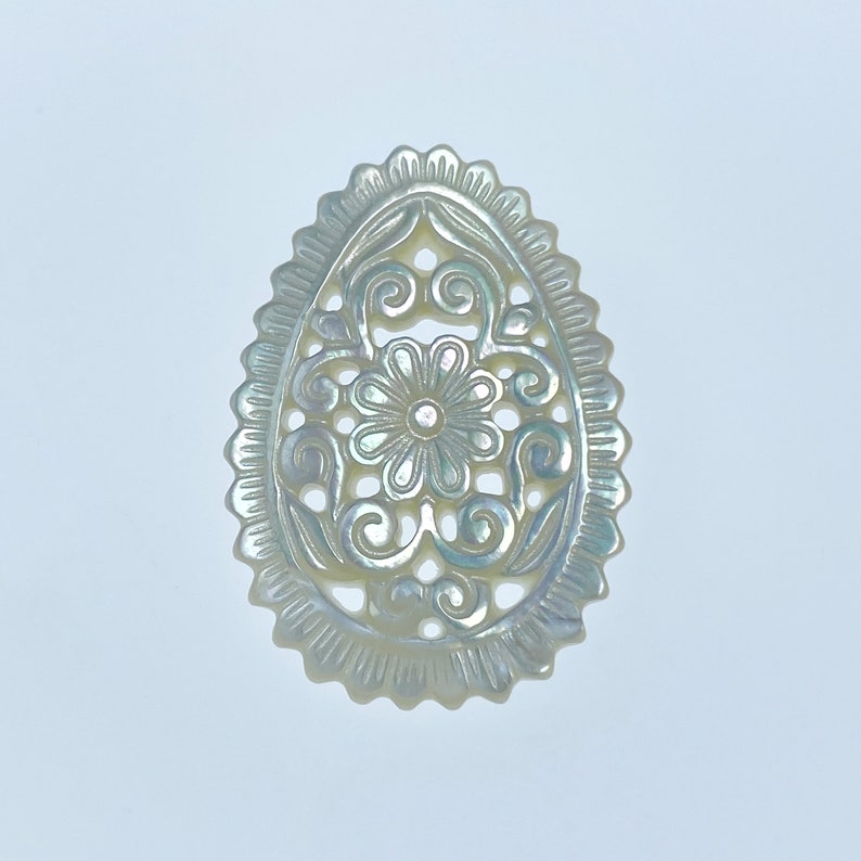 May include: A white oval-shaped mother of pearl pendant with a delicate floral design carved into it.