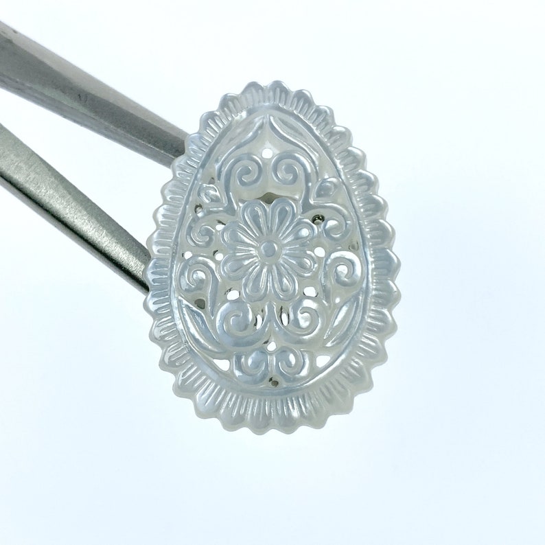 May include: A white oval-shaped mother of pearl pendant with a carved floral design.