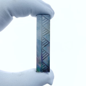 Puede incluir: Una caja rectangular plateada y azul con un patrón geométrico de triángulos. La caja está hecha de metal y tiene un acabado brillante.