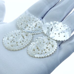 May include: Four white mother of pearl shell carvings with intricate floral designs. The carvings are oval shaped and have a smooth, polished finish.