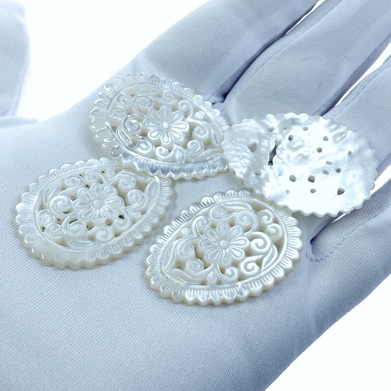 May include: Four white mother of pearl shell carvings with intricate floral designs. The carvings are oval shaped and have a smooth, polished finish.