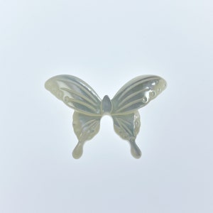May include: A white mother of pearl butterfly charm with intricate details. The butterfly is carved with delicate wings and a body.