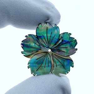 Peut inclure: Une fleur en nacre d'ormeau bleu et vert irisé avec un trou au centre. La fleur est sculptée en forme d'hibiscus.