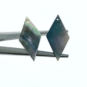 Puede incluir: Dos colgantes de concha de diamante negro iridiscente con un agujero en la parte superior para encordar.