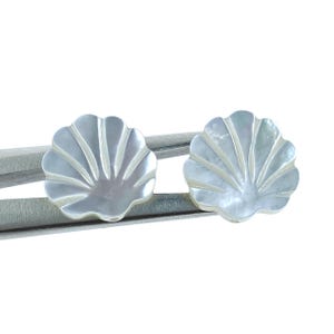 Peut inclure: Une paire de boucles d'oreilles en nacre blanche en forme de coquille. Les boucles d'oreilles sont en forme de coquille avec un bord festonné.