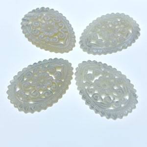 May include: Four white, oval-shaped, carved mother of pearl pendants with intricate floral designs.