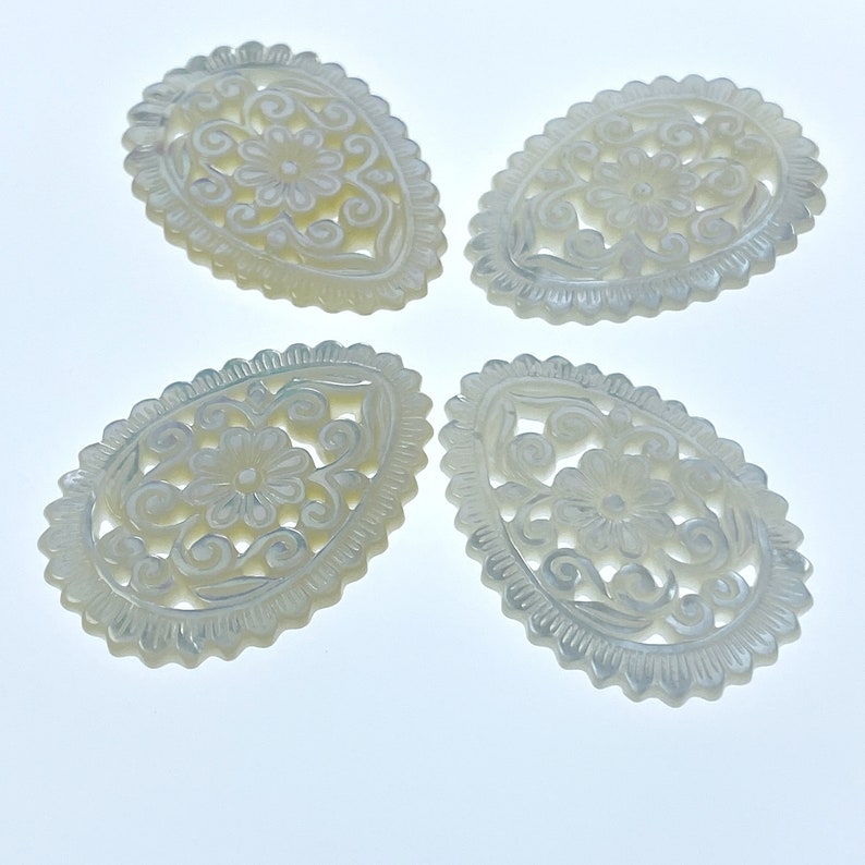May include: Four white, oval-shaped, carved mother of pearl pendants with intricate floral designs.