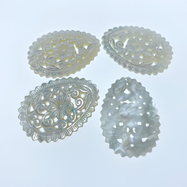 May include: Four white oval-shaped mother of pearl shell carvings with intricate floral designs. The carvings have a pearlescent sheen and are perfect for crafting or jewelry making.