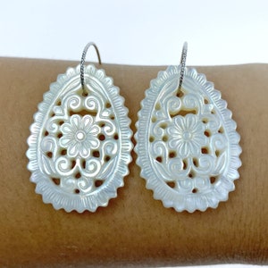 May include: A pair of white mother of pearl earrings with a floral design. The earrings are oval shaped and have a delicate, intricate pattern.