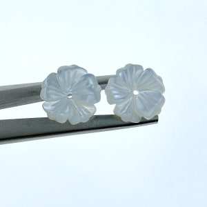 May include: Two white mother of pearl flower shaped buttons with a hole in the center.