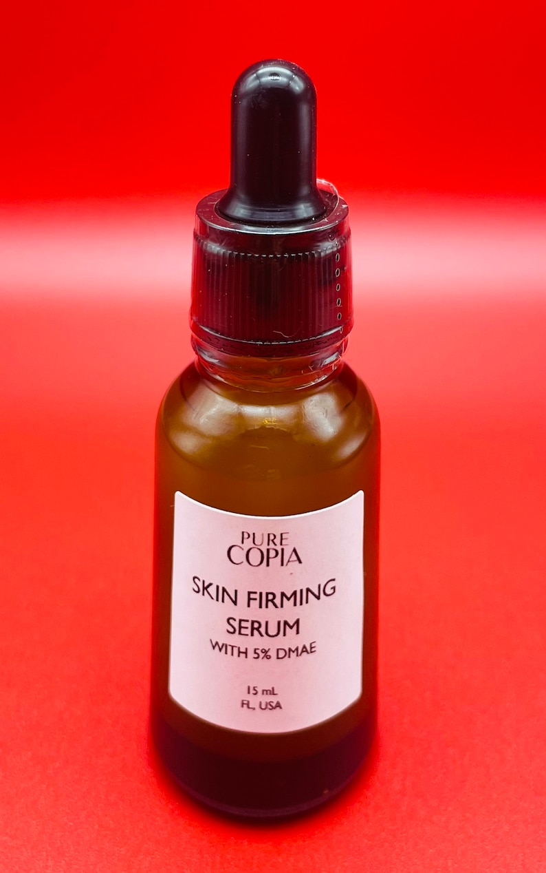 May include: A brown glass bottle with a black dropper top. The label reads "PURE COPIA SKIN FIRMING SERUM WITH 5% DMAE" and "15 mL FL, USA".