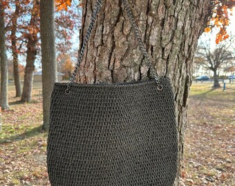 May include: A dark green crocheted tote bag with a silver chain strap hanging from a tree trunk.