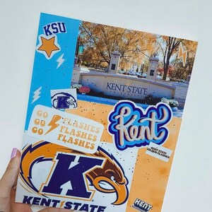 May include: A blue and gold Kent State University notebook with a variety of stickers, including a star, lightning bolts, and the words "Kent State Golden Flashes".