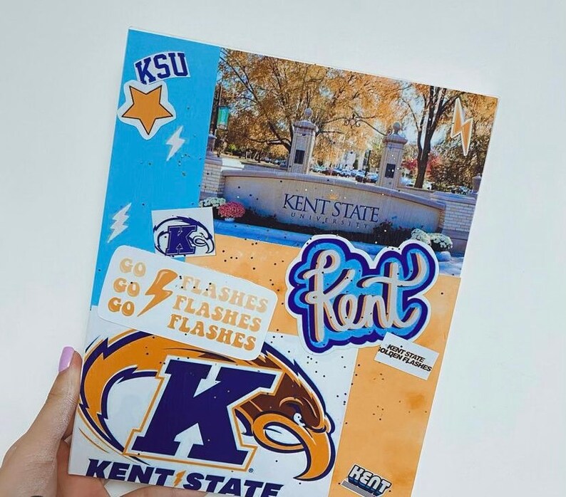 May include: A blue and gold Kent State University notebook with a variety of stickers, including a star, lightning bolts, and the words "Kent State Golden Flashes".