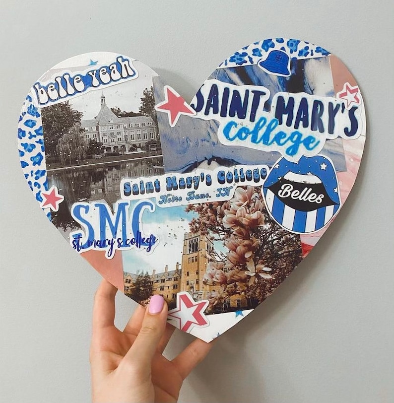 May include: A heart-shaped collage with blue, white, and red stickers and photos. The stickers include the text "Saint Mary's College", "SMC", "Belles", and "belle yeah". The photos show a building with a pond in front of it and a building with a magnolia tree in front of it.