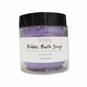 May include: A clear jar with a black lid filled with purple bath dough. The label reads "Sinarie natural soaps & skin care Bubble Bath Dough unscented net wt. 4 oz 113 g"
