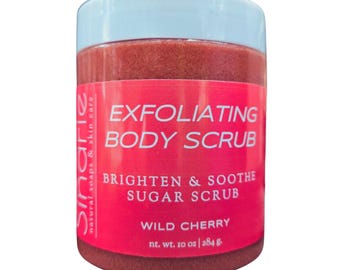 May include: A red jar of wild cherry sugar scrub with a white lid. The label reads "Exfoliating Body Scrub, Brighten & Soothe Sugar Scrub, Wild Cherry, nt. wt. 10 oz | 284 g".