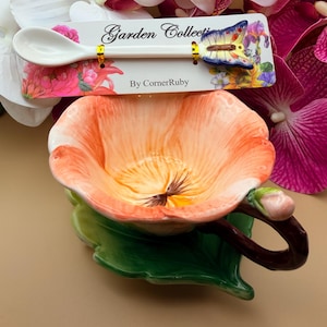 May include: A ceramic floral-shaped bowl with a green leaf base and a brown handle. A white spoon with a butterfly accent rests on top. The spoon is attached to a card that reads "Garden Collection" and "By CornerRuby."